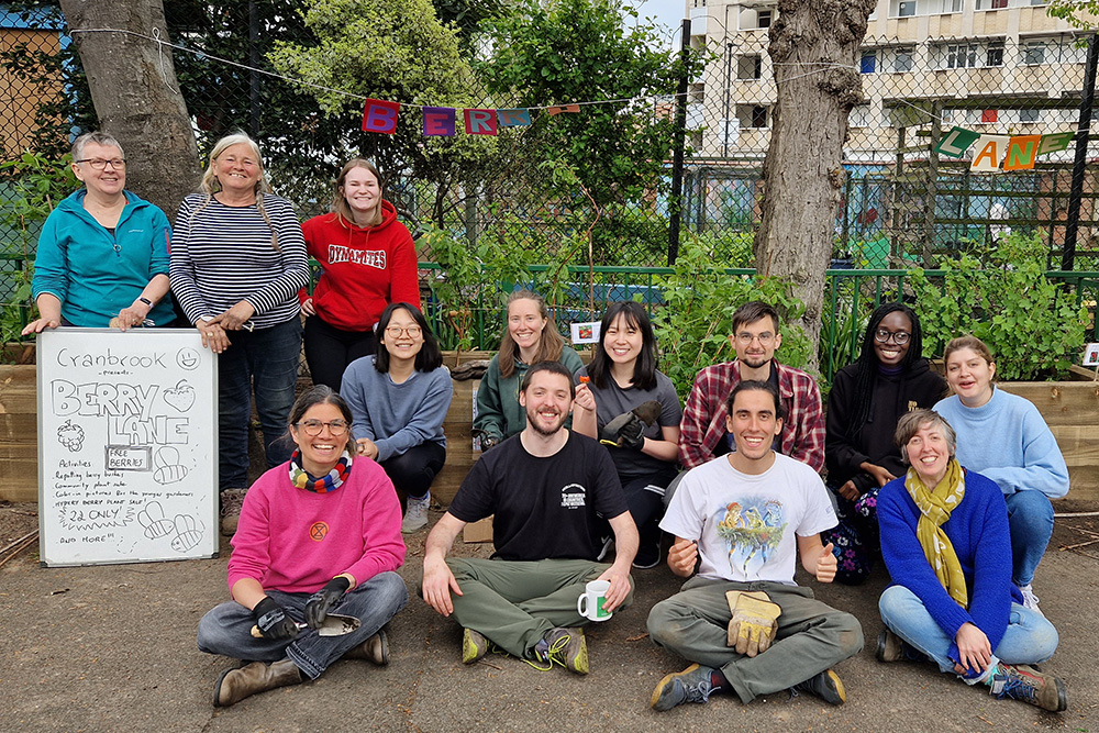 A mixed group of people smiling at the camera, sitting in front of one of a new fruit bush planter outside the garden fence.